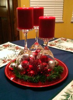 two candles are sitting on top of a red plate with christmas decorations and baubles