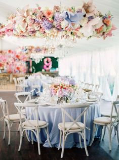 the tables are set up with white chairs and pink flowers hanging from the chandelier