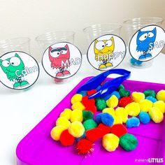 the plastic tray is filled with colorful pom poms and some cups are next to it