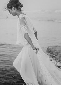 a woman in a white dress is walking on the beach with her hands in her pockets