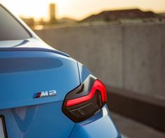 the rear end of a blue bmw car parked in front of a concrete wall with buildings in the background