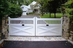 a white gate in front of a house with stone walls and trees around the entrance