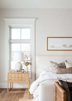 a bedroom with white walls and wood flooring has a wicker basket on the bed