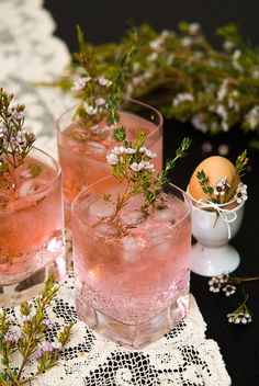 two glasses filled with pink liquid sitting on top of a lace doily next to an egg