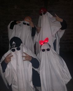 three people in white ghost costumes with red lights on their heads and hands covering their faces