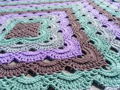 a crocheted blanket is laying on top of a tablecloth with purple and green squares