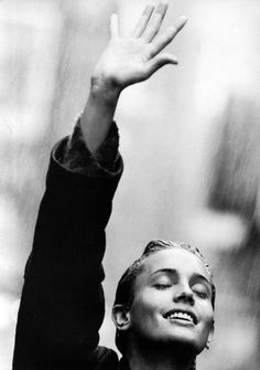 a black and white photo of a woman holding her hand up in the air while it rains