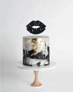 a white cake with black and gold decorations on top, sitting on a wooden stand