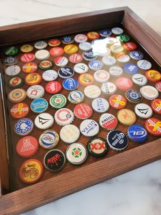 a wooden tray filled with lots of different types of bottlecaps on top of a marble counter