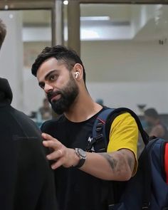 a man with ear buds on his ears is talking to another man in an airport