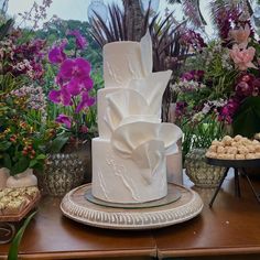 a large white cake sitting on top of a wooden table next to purple and pink flowers