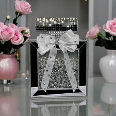 a box with pearls and a bow on the front sitting on a table next to pink roses