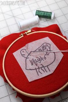 a red piece of cloth with some thread on it next to an embroidery hoop and spools of thread