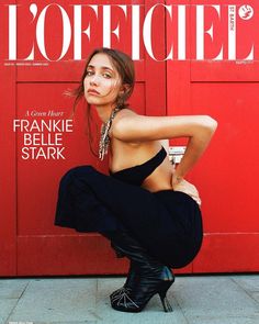 a woman sitting on the ground in front of a red door with her legs crossed