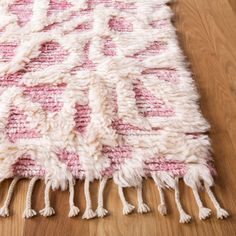 a pink and white rug with tassels laying on a wooden floor next to a wood floor