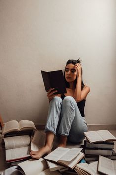 a woman sitting on the floor reading a book with books all around her and text reads, books you need to read this season