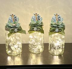 three glass jars with lights in them on a table