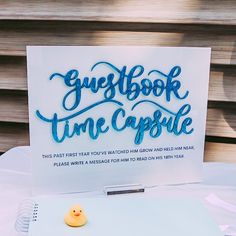 a sign that says guestbook time capsule with a rubber ducky on it sitting next to a notepad