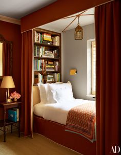 a bedroom with red curtains and a bed in the corner next to a book shelf