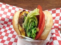 a hamburger with lettuce, tomato and cheese in a basket on a checkered table cloth