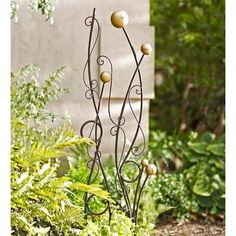 an iron planter with three balls on it in front of some bushes and trees