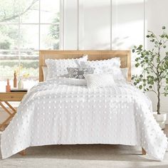 a bed with white comforter and pillows in a room next to a plant on the floor