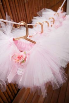 three pink tutu skirts hanging from a clothes line with gold hooks and flowers on them