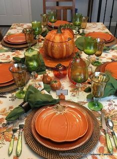 the table is set for thanksgiving dinner with pumpkins and green glassware on it