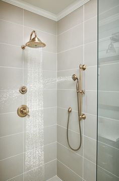 a shower head and hand held shower faucet in a white tiled bathroom with gold fixtures