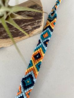 a close up of a beaded bracelet on a piece of wood with a plant in the background