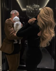 a man taking a photo of a woman holding a baby in front of a mirror