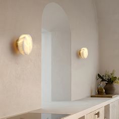 two lights on the side of a white wall next to a vase with flowers in it