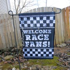 a black and white welcome race fans sign in front of a wooden fence with grass