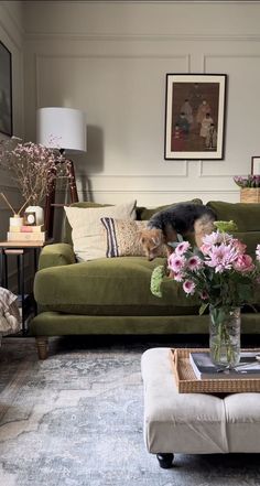 a dog laying on top of a couch next to a table with flowers in it