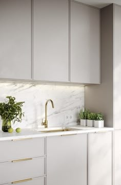 a white kitchen with marble counter tops and gold faucet pulls on the cabinet doors