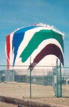 a large multicolored building behind a chain link fence on the side of a road