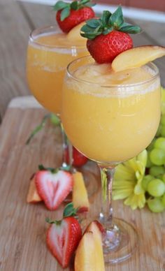 two glasses filled with fruit sitting on top of a wooden table