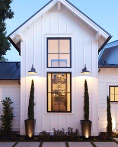 a white house with two large planters in front of the door and windows on each side