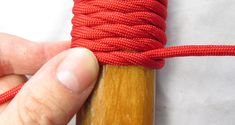 a hand holding a piece of red string on top of a wooden stick with an orange thread