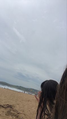 a woman standing on top of a sandy beach under a kite flying in the sky