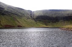 a large body of water surrounded by lush green hills and grass covered mountains in the distance