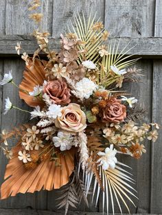 an arrangement of flowers and leaves on a wooden surface in front of a fence with wood slats