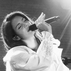 a woman singing into a microphone while wearing a white dress and holding her hands out