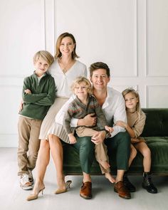 a family sitting on a green couch in front of white paneled walls, posing for the camera