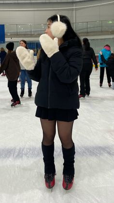 a woman is standing on an ice rink with her hands up to her face while wearing knee high boots