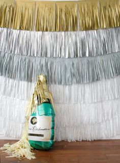 a bottle of champagne sitting on top of a wooden floor next to a string of gold and silver streamers