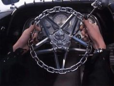 two hands on the wheel of an old car with chains hanging from it's center console