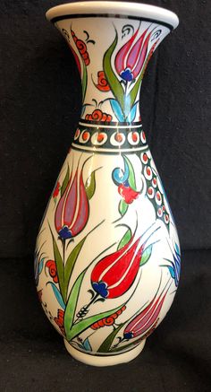 a white vase with colorful flowers painted on it's sides, sitting against a black background