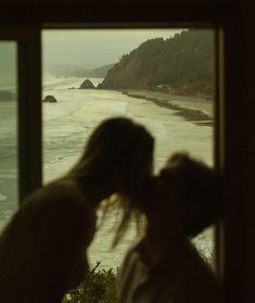 two people standing in front of a window looking out at the ocean