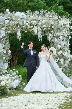 a bride and groom standing under an archway with white flowers